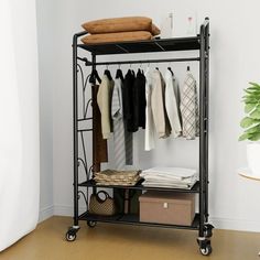 an iron rack with clothes hanging on it next to a potted plant in a white room