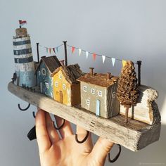 a hand holding a miniature model of a town on a piece of wood with flags hanging from it