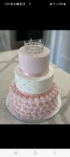 a three tiered cake is decorated with pink and white icing, topped with a tiara