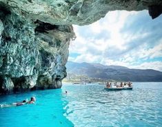 people swimming in the blue lagoon with boats and cliffs on the shore, while others swim nearby