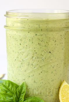 a mason jar filled with pesto sauce next to fresh basil leaves and a slice of lemon