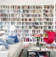 a living room filled with lots of books and furniture next to a wall full of books