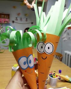 two paper carrots with googly eyes and green leaves on them, held up by someone's hand