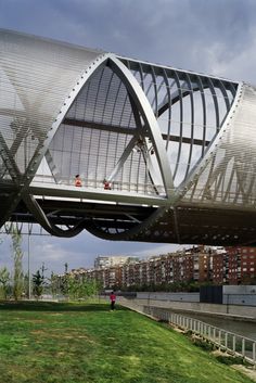 a person walking across a bridge over a body of water with buildings in the background