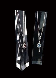 two necklaces are displayed in front of a clear display case on a black background