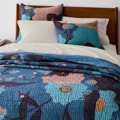 a bed with blue and pink flowers on the comforter, along with two pillows