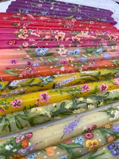 many different colored candles are lined up on a table with flowers and leaves painted on them