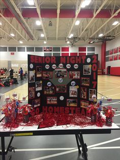 a table topped with pictures and confetti on top of a basketball court covered in red streamers