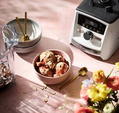 a bowl of food sitting on top of a table next to a blender and flowers