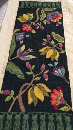 an embroidered table runner with flowers and leaves on black fabric, sitting on top of a white cloth