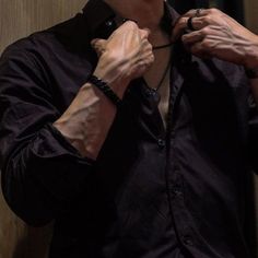 a man is adjusting his tie in front of a mirror while wearing a black shirt