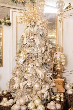 a white christmas tree with gold and silver ornaments in baskets on the floor next to it