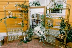 a table topped with lots of glasses next to a yellow wall covered in greenery