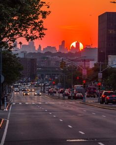 the sun is setting over a city street with cars on it and buildings in the background