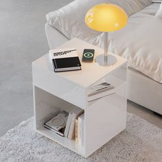 a white table with a lamp and books on it in front of a couch,