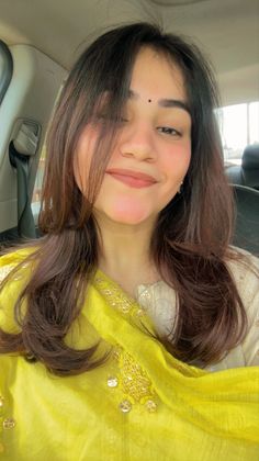 a woman sitting in the back seat of a car wearing a yellow shawl and smiling