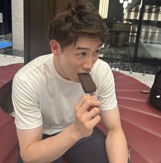 a young man sitting on a bench eating an ice cream bar