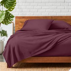 a bed with purple sheets and pillows on top of it next to a potted plant