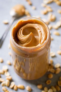 peanut butter in a glass jar with peanuts scattered around it and a spoon on the side