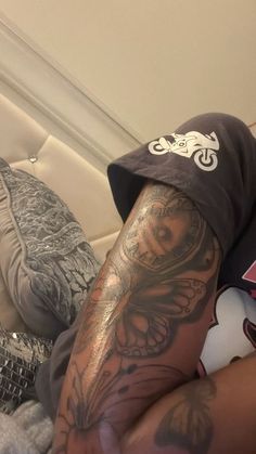 a man with tattoos on his arm laying in bed next to a pillow and pillows