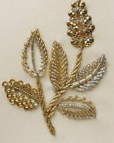 gold and silver leaf brooch pins on white fabric background with text overlay that reads,'tila embroiderry '