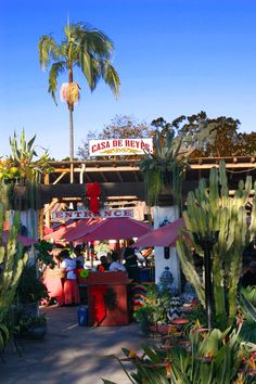 a restaurant with palm trees in the background and people sitting at tables under umbrellas