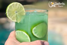 a hand holding a green drink with lime slices