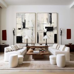 a living room filled with white couches and two large paintings on the wall above them