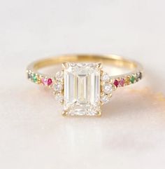 an emerald cut diamond ring with multi - colored stones on the band and side stones