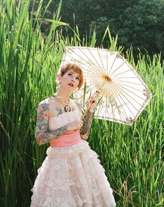 a woman with tattoos holding an umbrella in front of some tall grass and plants,