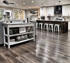 a large open concept kitchen and living room with wood flooring, white cabinets and bar stools