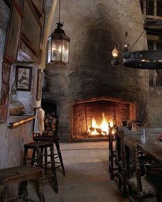 a fireplace in a stone walled room with wooden tables and stools next to it