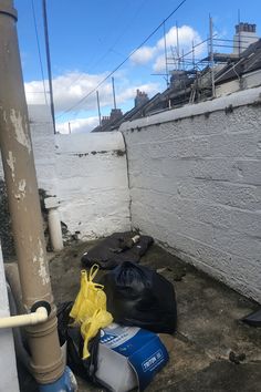 trash bags and other items are on the ground next to a white wall with scaffolding