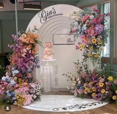 a cake sitting on top of a white table surrounded by colorful flowers and greenery