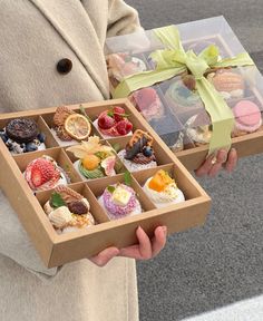 a person holding an open box filled with different types of pastries and desserts