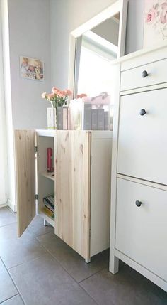 a white dresser sitting next to a window with flowers in the vase on top of it