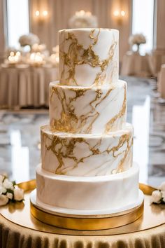 a three tiered white and gold marbled cake on a table with candles in the background