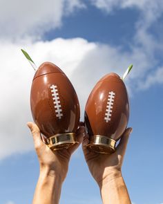 two hands holding up footballs against a blue sky