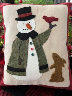 a pillow with a snowman holding a bird on it's arm and a dog standing next to it