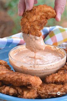 a person dipping something into a bowl of sauce on chicken nuggies in a blue bowl