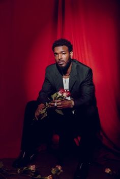 a man sitting in front of a red curtain holding flowers and looking at the camera