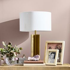 a table with a lamp, pictures and flowers on it in front of a pink wall