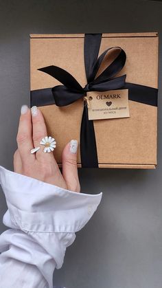 a woman's hand holding a gift box with black ribbon and white flowers on it