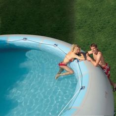 two people are sitting on the edge of a swimming pool and one person is holding onto an object