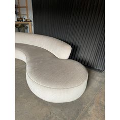 a curved couch sitting on top of a cement floor next to a black metal wall