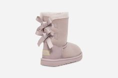 We added sweet silky bows to your little one's favorite boot, but kept the super-soft sheepskin feel they love. Built to move the way kids do, each boot features a rocker-bottom shape for a barefoot feel and our ultra-lightweight outsole for traction and durability. Pair with the same style in our women's sizes for cute mini-me moments.The outsole of this product is either a sugarcane EVA outsole, which is a responsible compound using sugarcane foam that allows us to reduce dependency on fossil fuels by replacing petroleum-based ethylene, or a Treadlite by UGG® outsole.This product was made in a factory that supports women in our supply chain with the help of HERproject. This collaborative initiative creates partnerships with brands like ours to empower and educate women in the workplace. Ugg Boots With Bows, Ugg Booties, Ugg Store, Mini Baileys, Bailey Bow, Kids Uggs, Favorite Boots, Classic Boots, Slipper Shoes