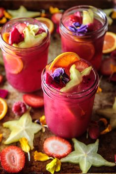 three jars filled with fruit and flowers on top of a wooden table next to sliced oranges