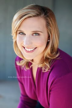 a woman with blonde hair and blue eyes smiles at the camera while wearing a purple shirt