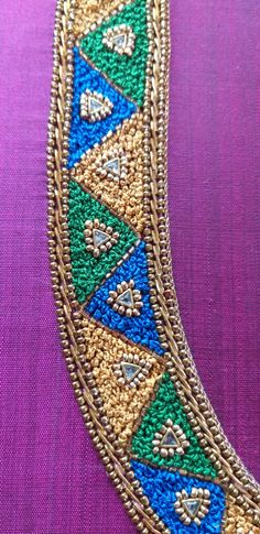 a gold and blue beaded bracelet on a purple cloth with an orange flower in the center