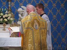 two men standing next to each other in front of a priest at a table with flowers